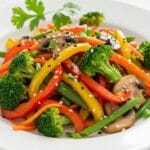 Colorful Broccoli and Mushroom Stir Fry with bell peppers, carrots, sesame seeds, and green onions on a white plate