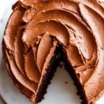 Close-up of a chocolate cake with creamy frosting and a slice cut out revealing soft, moist layers.