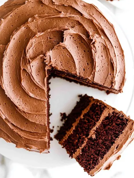 A top-down view of a chocolate cake with a slice cut to reveal soft layers inside