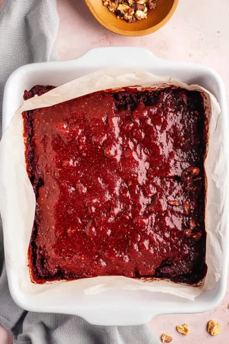 Rich red velvet brownie batter swirled with vibrant red topping in a white baking dish, ready to bake.