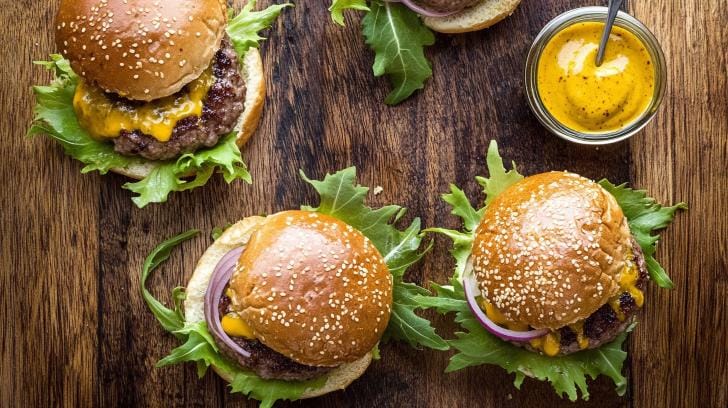 Delicious Beef smash Burger with melted cheese, fresh lettuce, and vibrant red onions on a rustic wooden board.