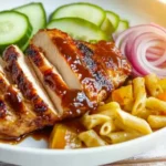 Sliced BBQ chicken breast with pasta, cucumbers, and red onion, showing delicious serving suggestions.