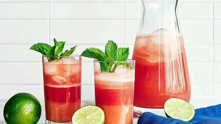 Two tall glasses and a pitcher filled with icy watermelon juice, garnished with mint and lime.