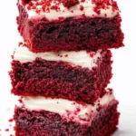 Stack of three red velvet brownie squares with creamy white frosting and red crumbs on top.