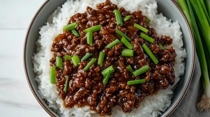 Overhead view of Mongolian ground beef with fresh scallions, served atop a generous bed of white rice.