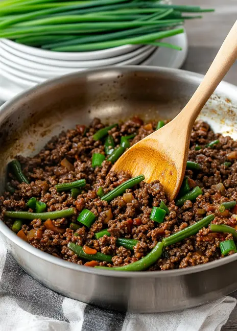Sizzling Mongolian ground beef with vibrant green beans and chopped scallions in a stainless steel pan, ready to serve.