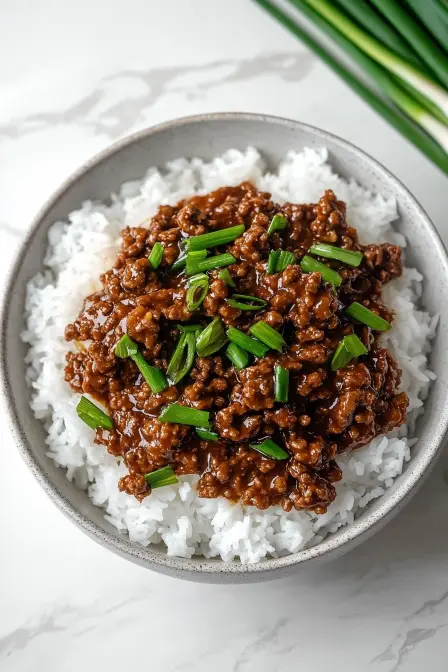 Top-down view of savory Mongolian ground beef with scallions, served over fluffy white rice in a bowl.