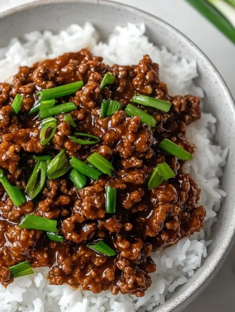 Close-up of rich Mongolian ground beef, glazed and topped with fresh green onions, served over white rice.