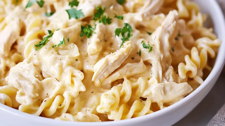 Close-up of creamy crockpot garlic parmesan chicken pasta with shredded chicken and parsley