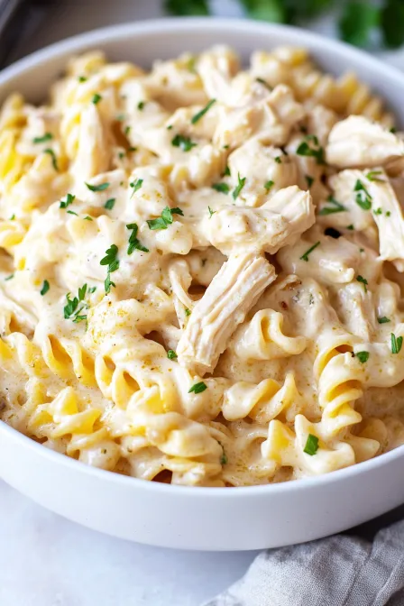 Side view of crockpot garlic parmesan chicken pasta in a white bowl with creamy sauce and parsley