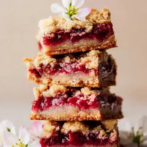 Stack of golden brown strawberry rhubarb crumb bars topped with a flower, showcasing their juicy filling.