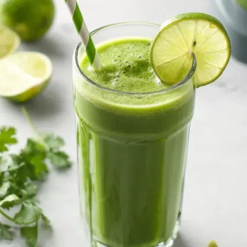 Refreshing green detox smoothie with lime and herbs, served chilled in a tall glass with striped straw.