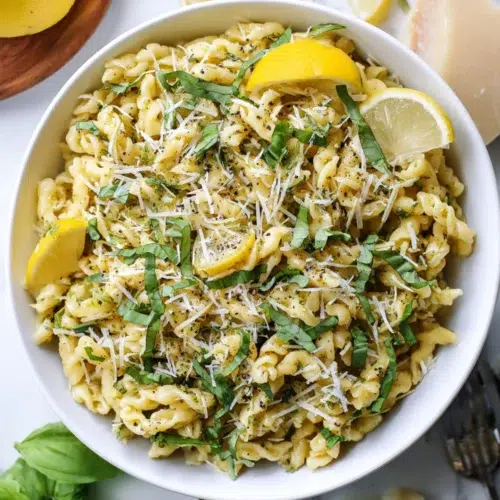Lemon basil pasta salad topped with shredded parmesan, fresh basil, and cracked black pepper in a white bowl.