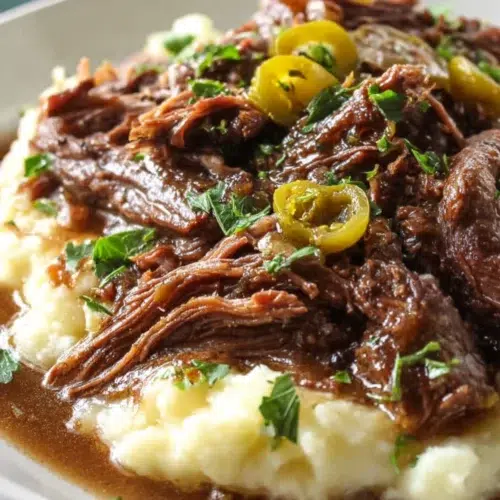 Close-up of tender Mississippi pot roast with gravy and pepperoncini, served over creamy mashed potatoes with fresh parsley.