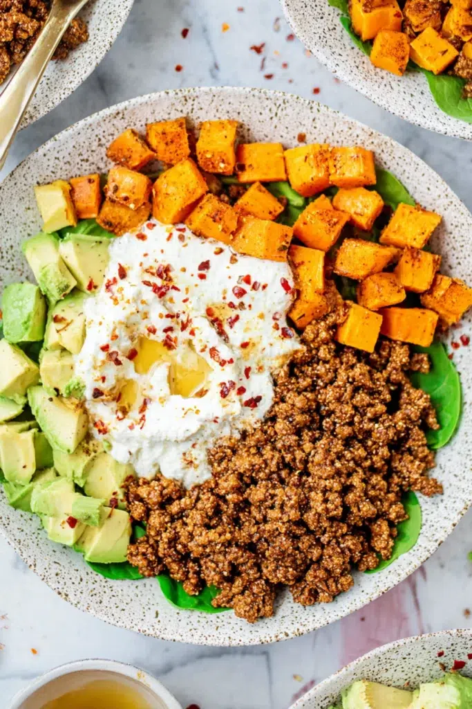 Power bowl with ground beef, roasted sweet potatoes, avocado chunks, and whipped ricotta topped with chili flakes