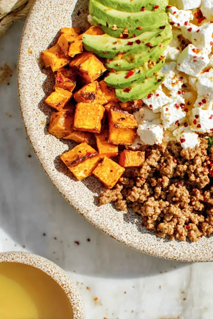 Power bowl with roasted sweet potatoes, avocado slices, crumbled feta, and seasoned ground beef topped with chili flakes