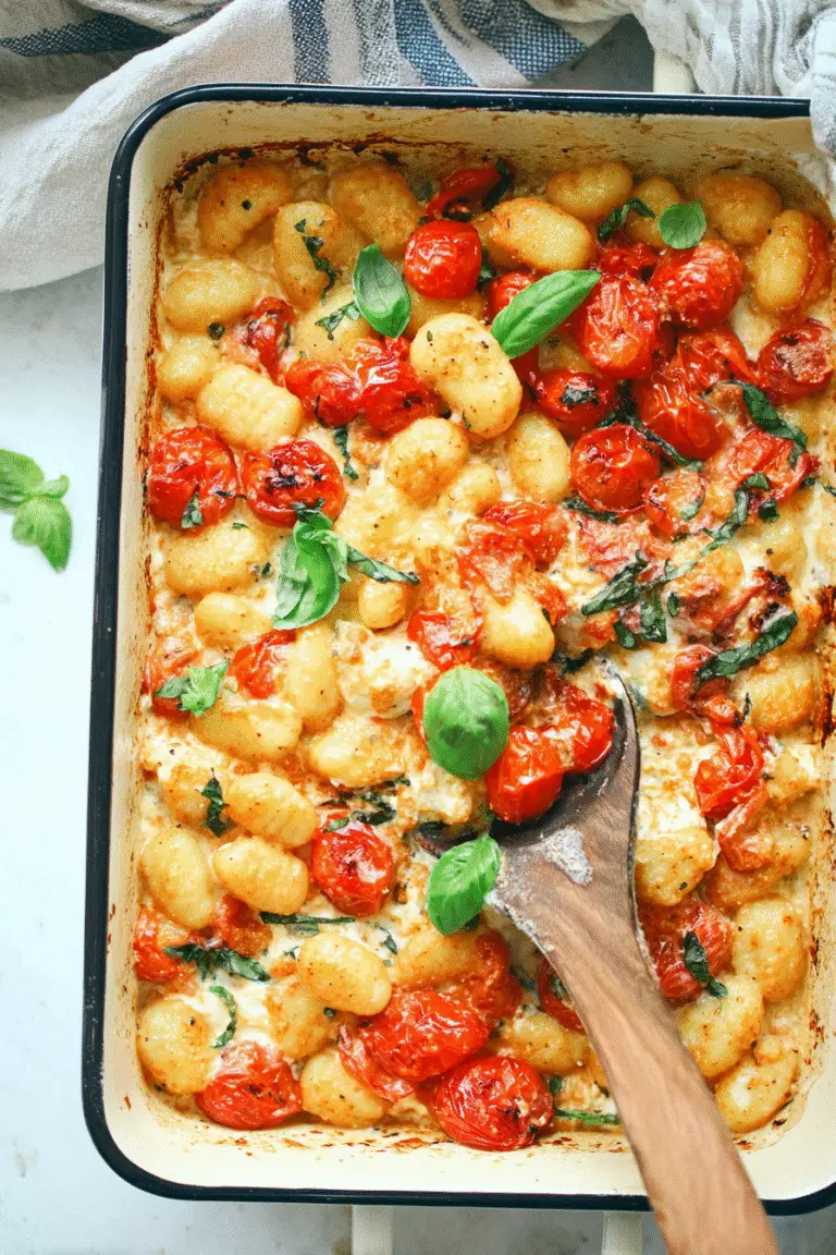 Golden baked feta gnocchi with roasted cherry tomatoes, fresh basil, and creamy cheese in a baking dish.
