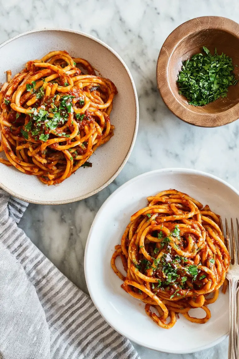 Overhead view of two bowls of caramelized shallot pasta topped with parsley, served on a marble table with fresh herbs