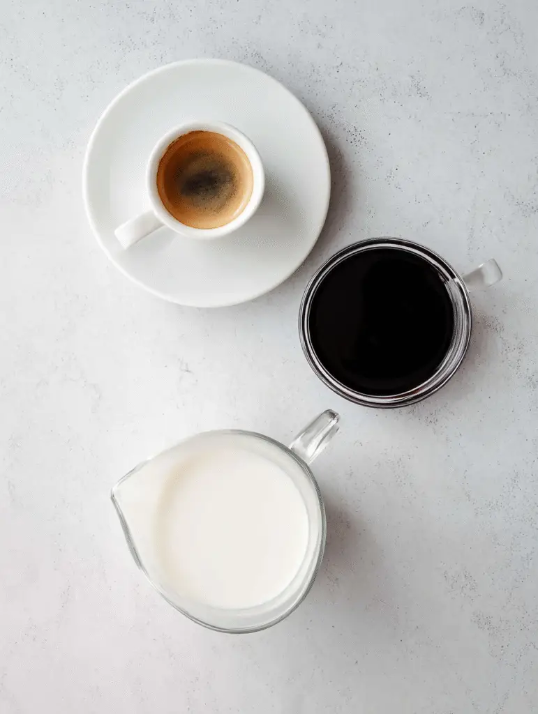 Flat lay of espresso shot, blueberry syrup, and milk in clear cups on a white background for iced blueberry latte recipe