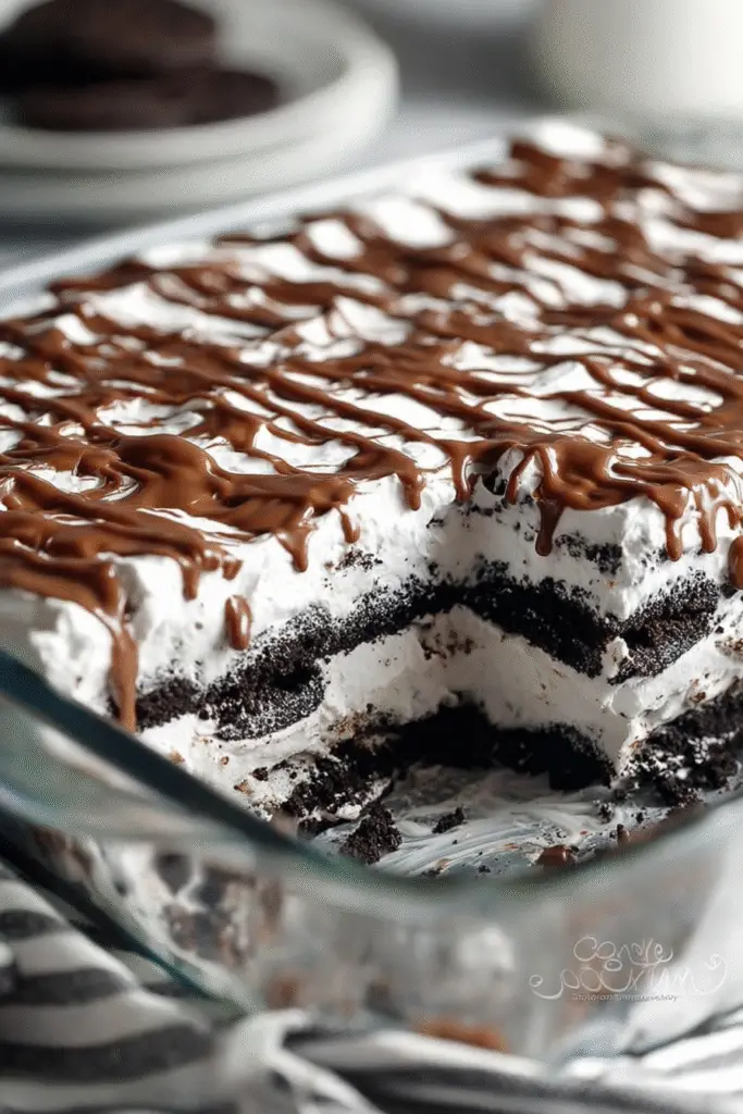 Rich layers of Oreo crumbs and fluffy cream topped with chocolate drizzle in a glass dish, ready to serve