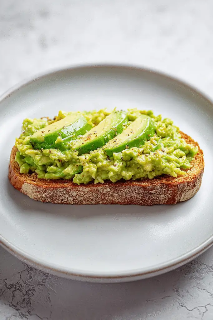 Toasted bread topped with creamy mashed avocado and fresh avocado slices, sprinkled with black pepper for extra flavor