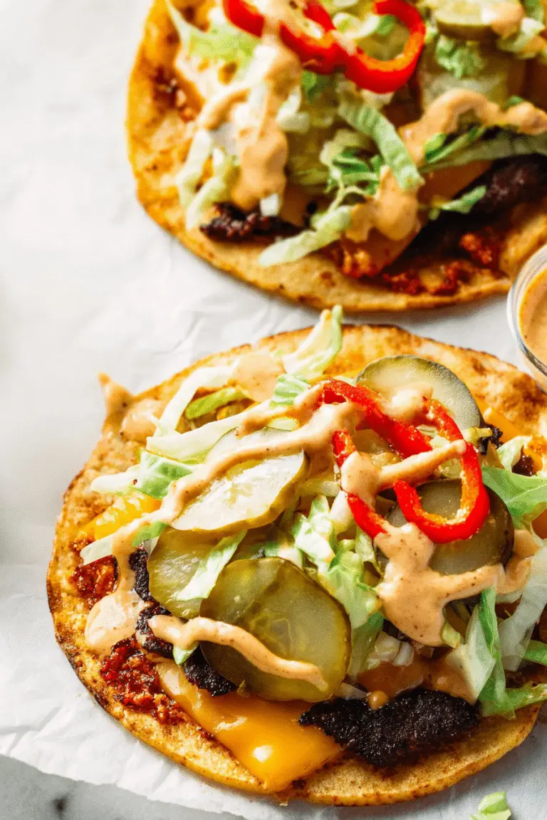 "Two smash burger tacos on golden tortillas topped with melted cheese, lettuce, pickles, red peppers, and chipotle sauce"