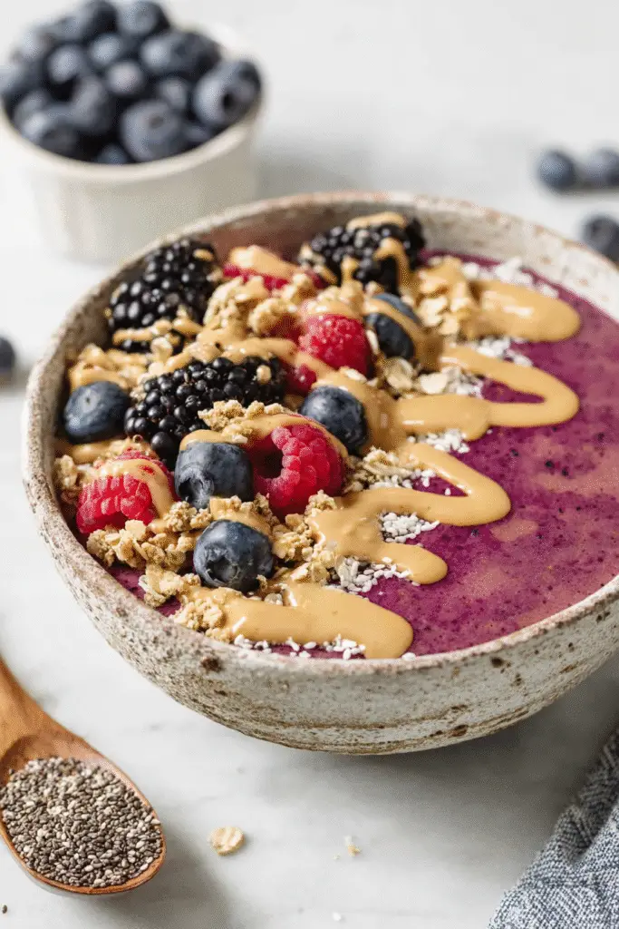 Smoothie bowl with blueberries, raspberries, blackberries, granola, chia seeds, and peanut butter drizzle on top