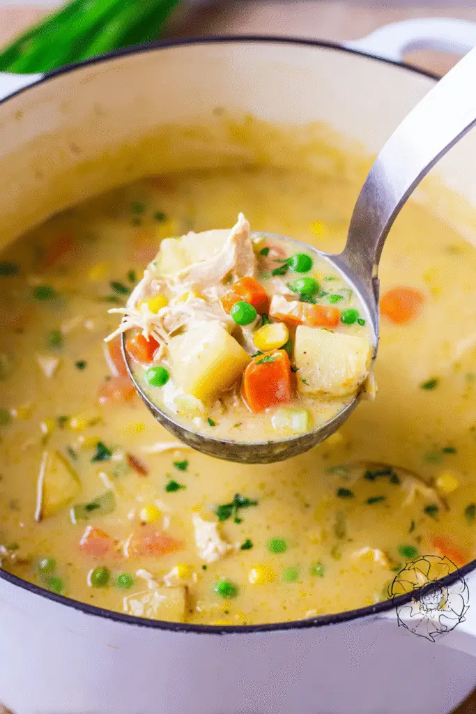 Chicken Pot Pie Soup in a white Dutch oven pot, creamy golden broth filled with tender chunks of chicken,