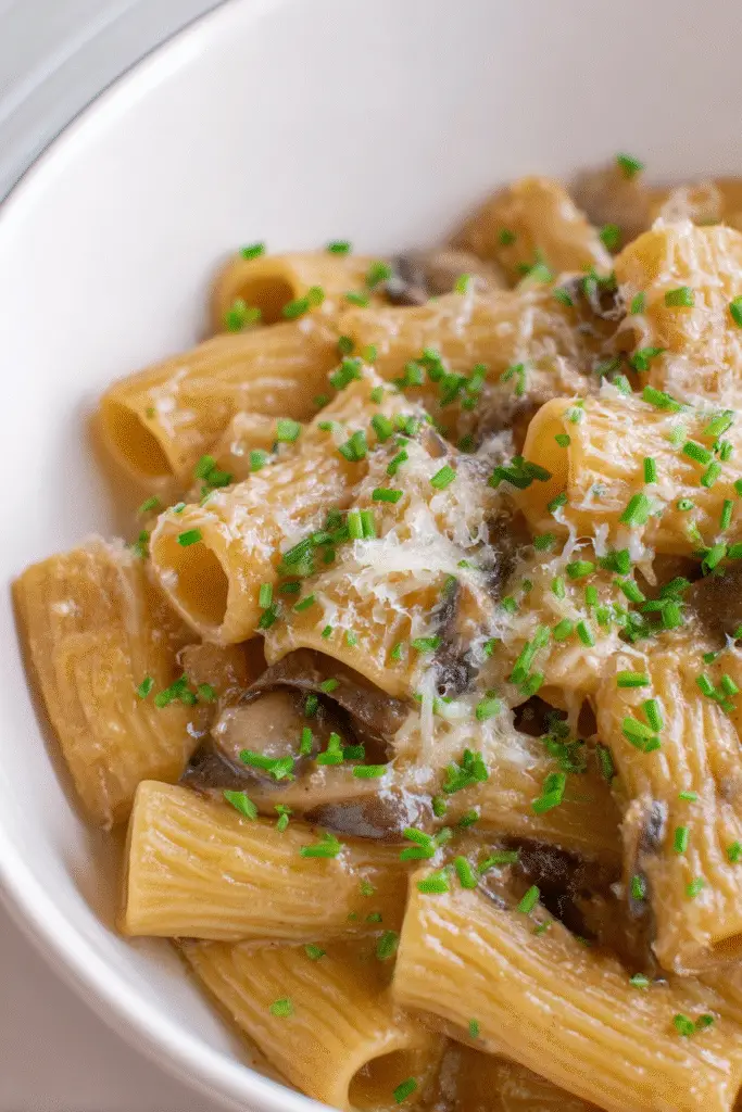 French Onion Pasta Soup, rigatoni pasta coated in a rich caramelized onion and mushroom sauce, topped with melted cheese and sprinkled with fresh chives, hyper-realistic food photography