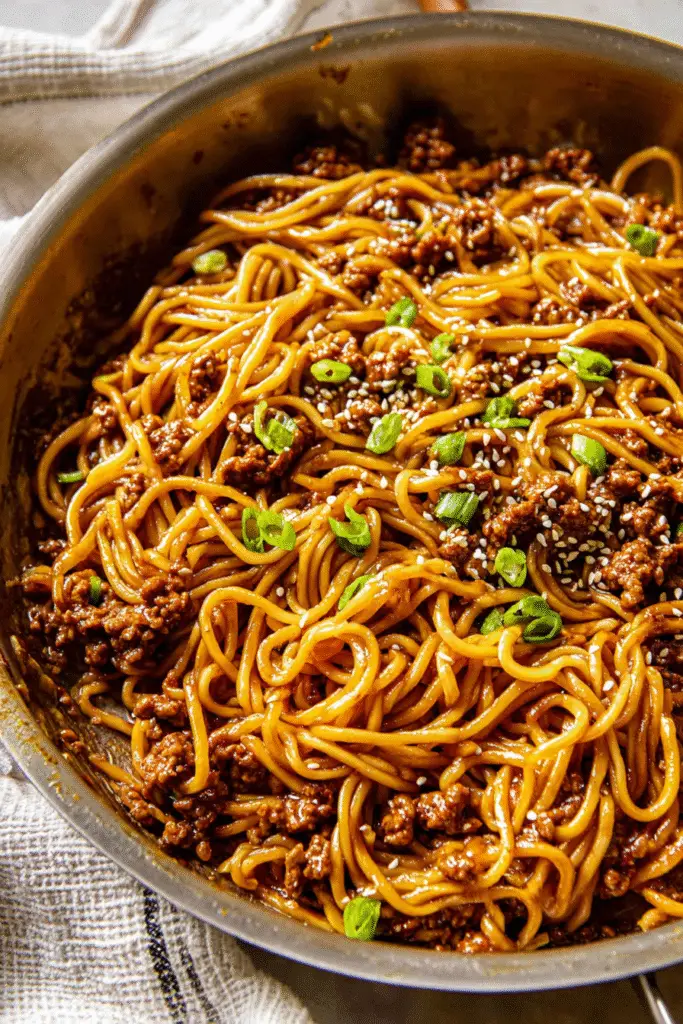 Savory Mongolian ground beef noodles coated in rich soy-ginger sauce with scallions and sesame seeds in a skillet