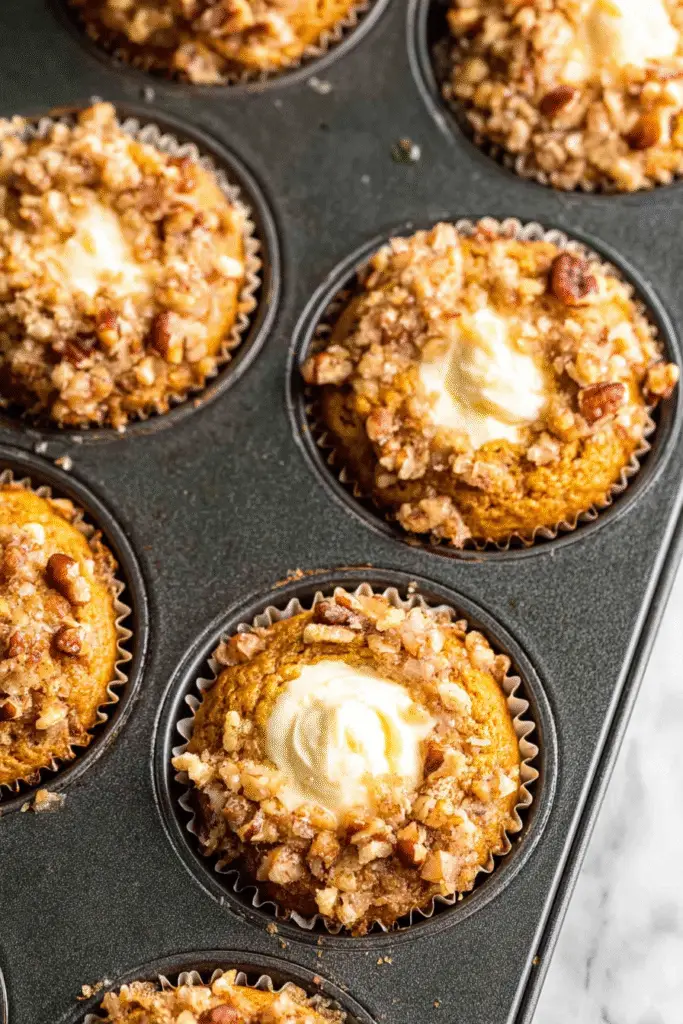 Warm pumpkin cream cheese muffins with creamy centers and nutty streusel topping in a dark muffin pan