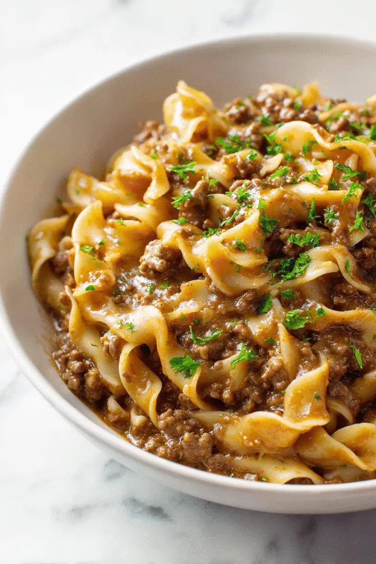 Tender egg noodles tossed with rich beef gravy and ground beef, garnished with fresh parsley for a cozy dinner