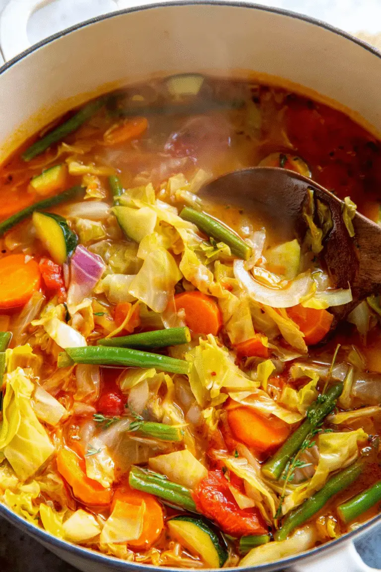 Colorful cabbage soup simmering with carrots, green beans, zucchini, and onions in a flavorful tomato broth