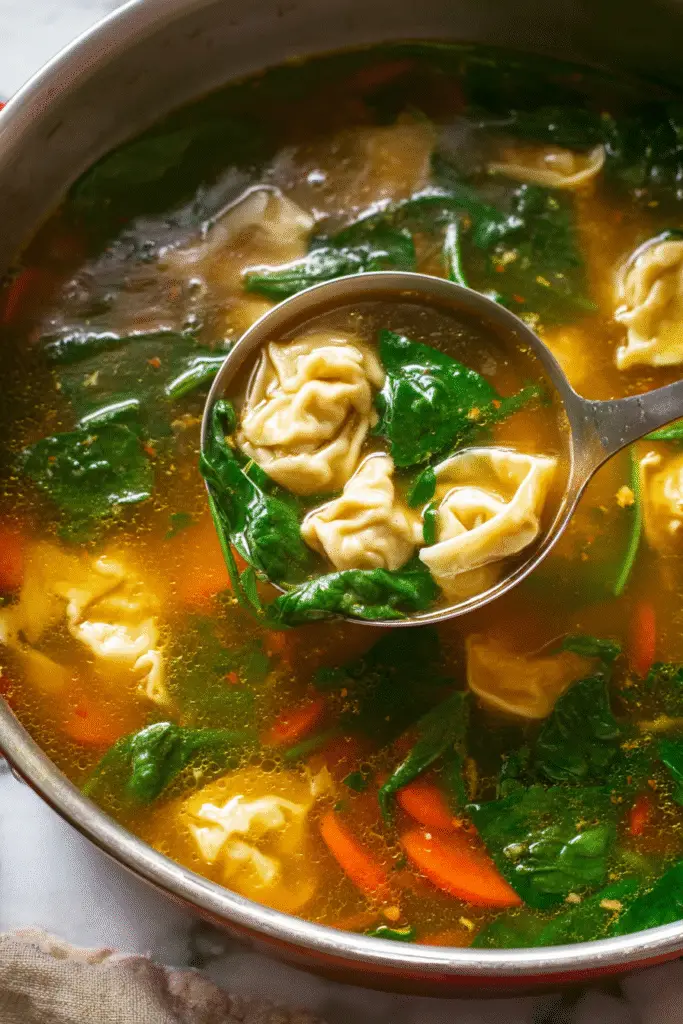 Ladle serving quick and easy wonton soup with spinach, carrots, and tender wontons in clear golden broth.
