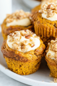 Fluffy pumpkin muffins filled with creamy cheesecake center topped with streusel crumbs on a white plate