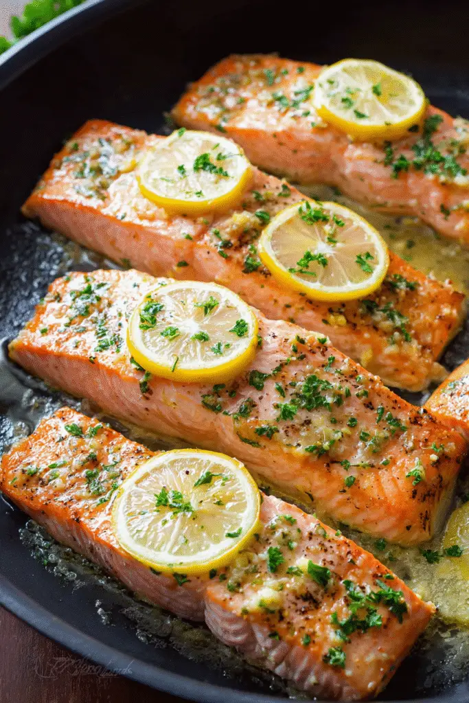 Baked Dijon salmon fillets in a skillet topped with lemon slices and parsley, cooked to golden perfection.
